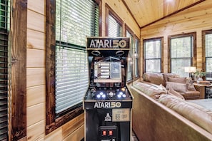 A room with a vintage Atari 50 arcade machine, a leather sofa, and wooden paneled walls. - Hike, Soak & Play! Luxe Broken Bow Escape (Broken Bow)
