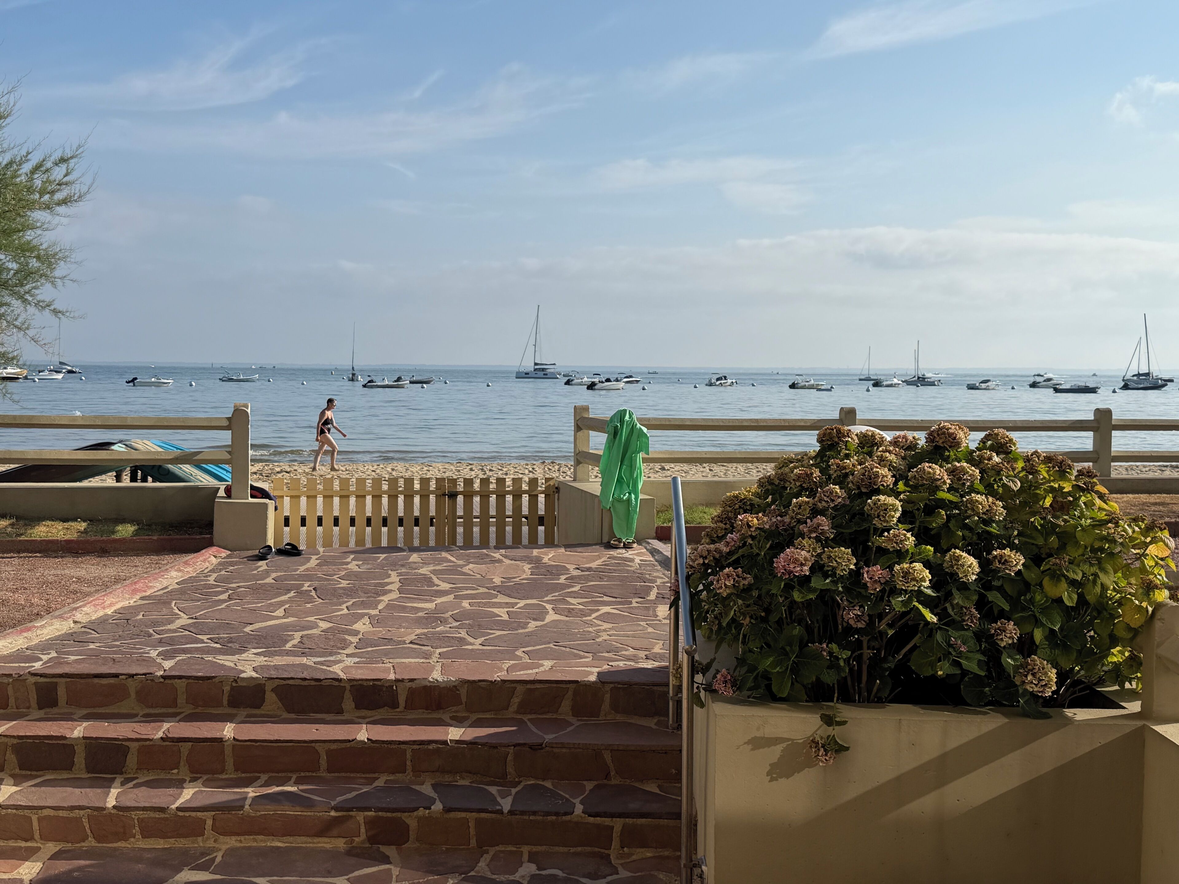 A stone-paved walkway leading to a beach with boats in the water.