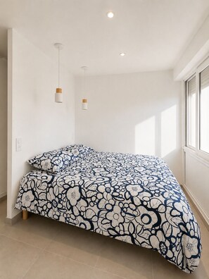 A bedroom with a large bed, two pendant lights, and a window providing natural light. - Renovated one-bedroom apartment on the Arcachon Bay, right on the beach (Arcachon)