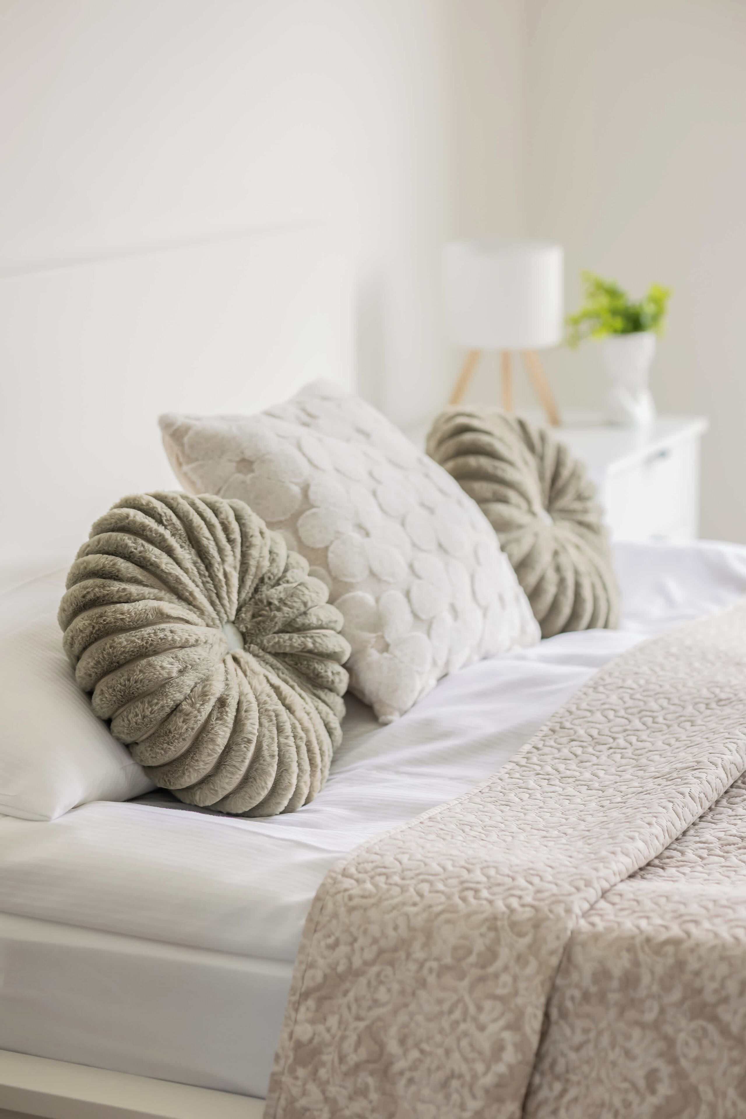 A bed with a white headboard, a beige throw blanket, and two decorative pillows with a textured pattern.