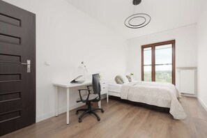 Ein Schlafzimmer mit Bett, Schreibtisch mit Stuhl, Fenster und Tür.