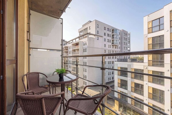 A balcony with wicker chairs, a small round table, and a potted plant. - Air-Conditioned 3 Bedroom Apartment in Warsaw by Noclegi Renters (Warszawa)