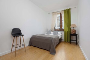A small, well-lit bedroom with a single bed, a chair, a nightstand, and a lamp. - Air-Conditioned 3 Bedroom Apartment in Warsaw by Noclegi Renters (Warszawa)