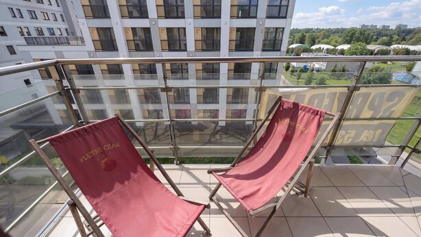 En balkong med två röda solstolar och ett glasräcke med utsikt över stadsbilden.
