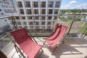 A balcony with two red lounge chairs and a glass railing overlooking a cityscape. - Air-Conditioned 3 Bedroom Apartment in Warsaw by Noclegi Renters (Warszawa)