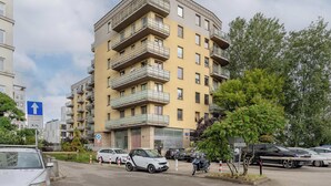 En flervåningsbyggnad med bostäder, balkonger, parkerade bilar och en klar himmel.