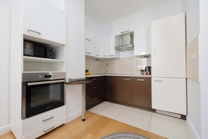A compact kitchen with white cabinetry, a built-in oven, a microwave, and a stainless steel range hood. - Air-Conditioned 3 Bedroom Apartment in Warsaw by Noclegi Renters (Warszawa)