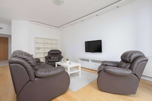 Un salon moderne avec des canapés en cuir, une table basse blanche et un téléviseur à écran plat fixé au mur.
