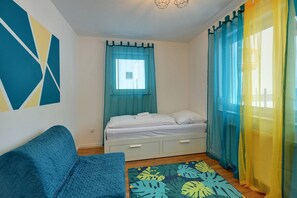 Ein Schlafzimmer mit einem Bett, einem blauen Sofa, einem Fenster mit Vorhängen und einem geometrischen Wandmuster.