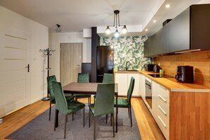 Eine kompakte Küche mit Essbereich, ausgestattet mit einem Holztisch, grünen Stühlen und einer modernen Leuchte.
