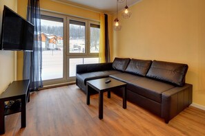 Ein modernes Wohnzimmer mit einer Ledersofa, einem Couchtisch, einem Fernseher und großen Fenstern mit Vorhängen.