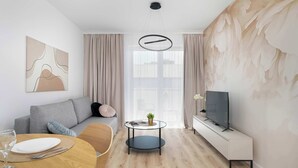Una sala moderna con un sofá, una mesa de comedor, un televisor y un amplio ventanal con cortinas.