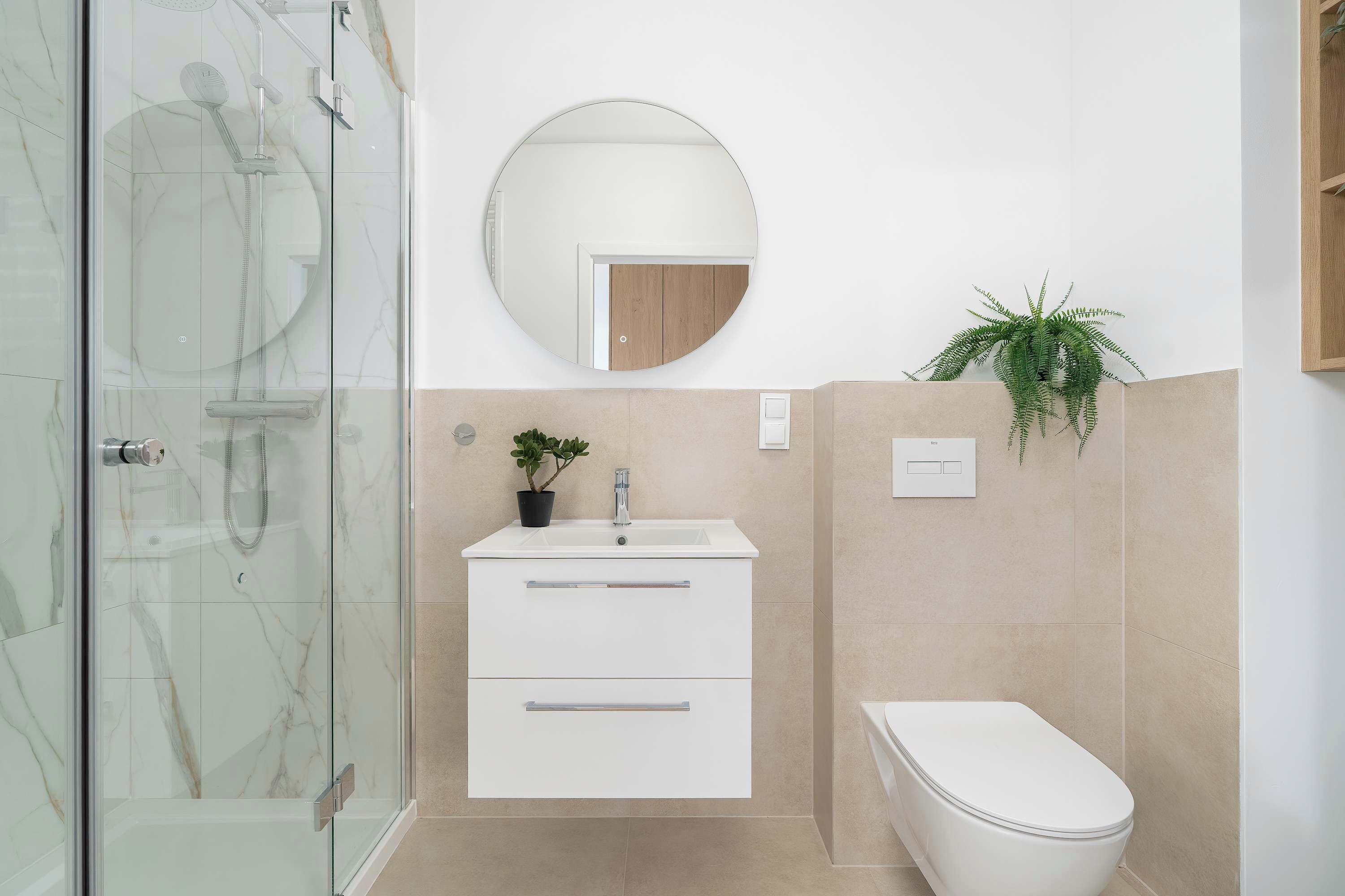 A modern bathroom with a glass shower enclosure, a white sink with a mirror above, and a toilet.