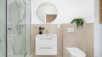 A modern bathroom with a glass shower enclosure, a white sink with a mirror above, and a toilet.