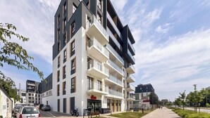 Un edificio residencial de varios pisos con balcones, una entrada visible y un cielo despejado.
