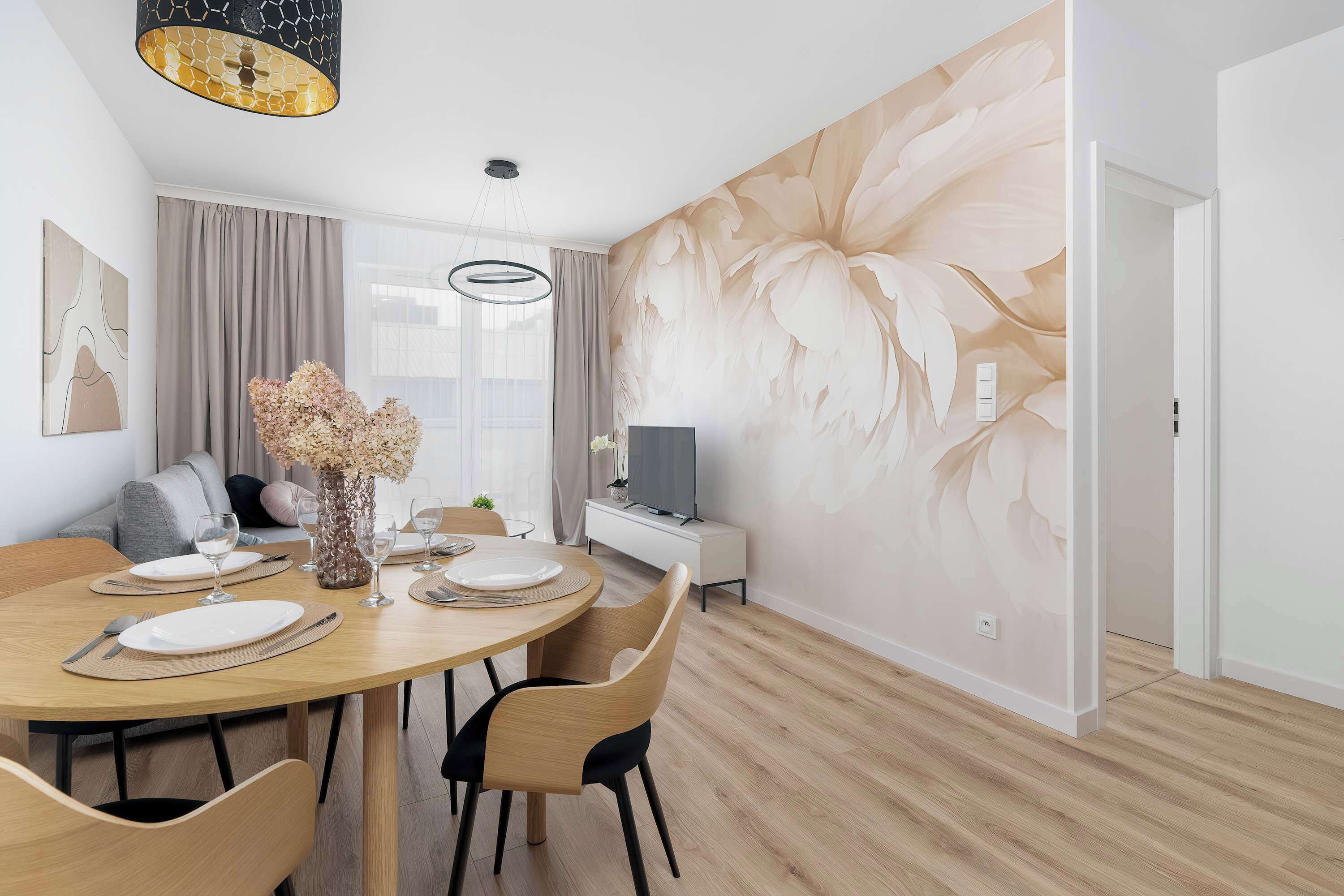A modern dining area with a round wooden table, chairs, and a vase of flowers.