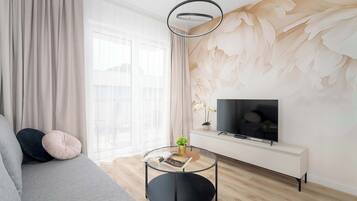 En moderne stue med sofa, rundt sofabord, TV på hvidt skab og stort vindue med lette gardiner.