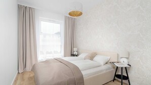 Un dormitorio moderno con una cama grande, una mesita de noche con lámpara y una ventana con cortinas.