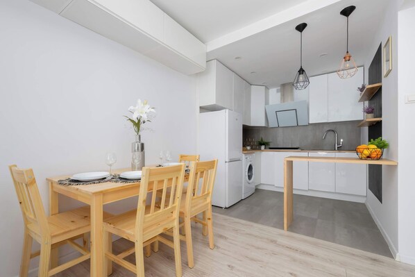 Una cocina moderna con armarios blancos, una mesa de comedor con sillas y una lámpara colgante.