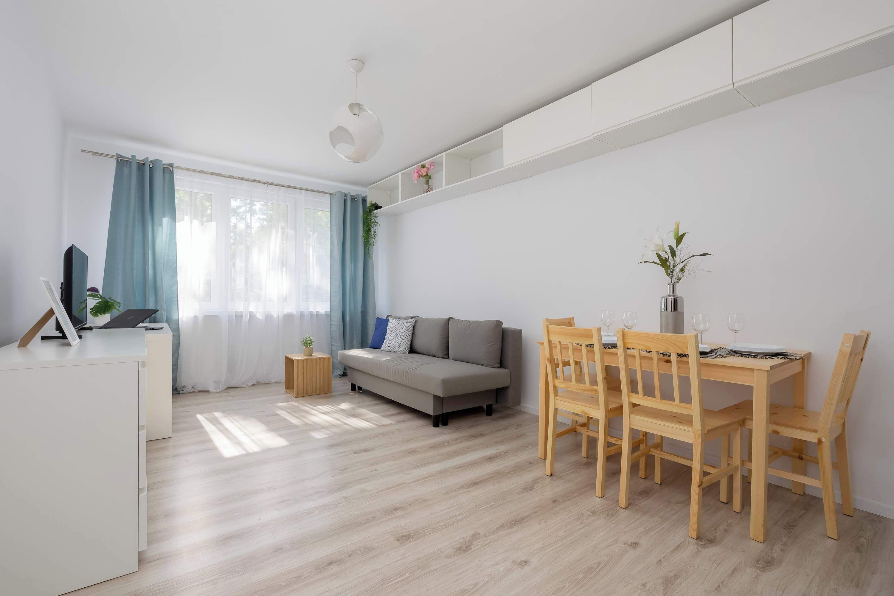 A modern living room with a sofa, dining table, chairs, and a TV on a stand.