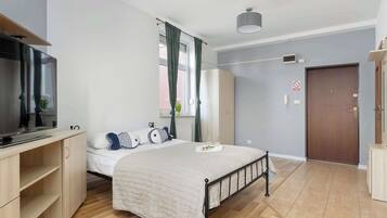 Een slaapkamer met een bed, televisie, bureau, kledingkast, een deur en een raam met gordijnen.