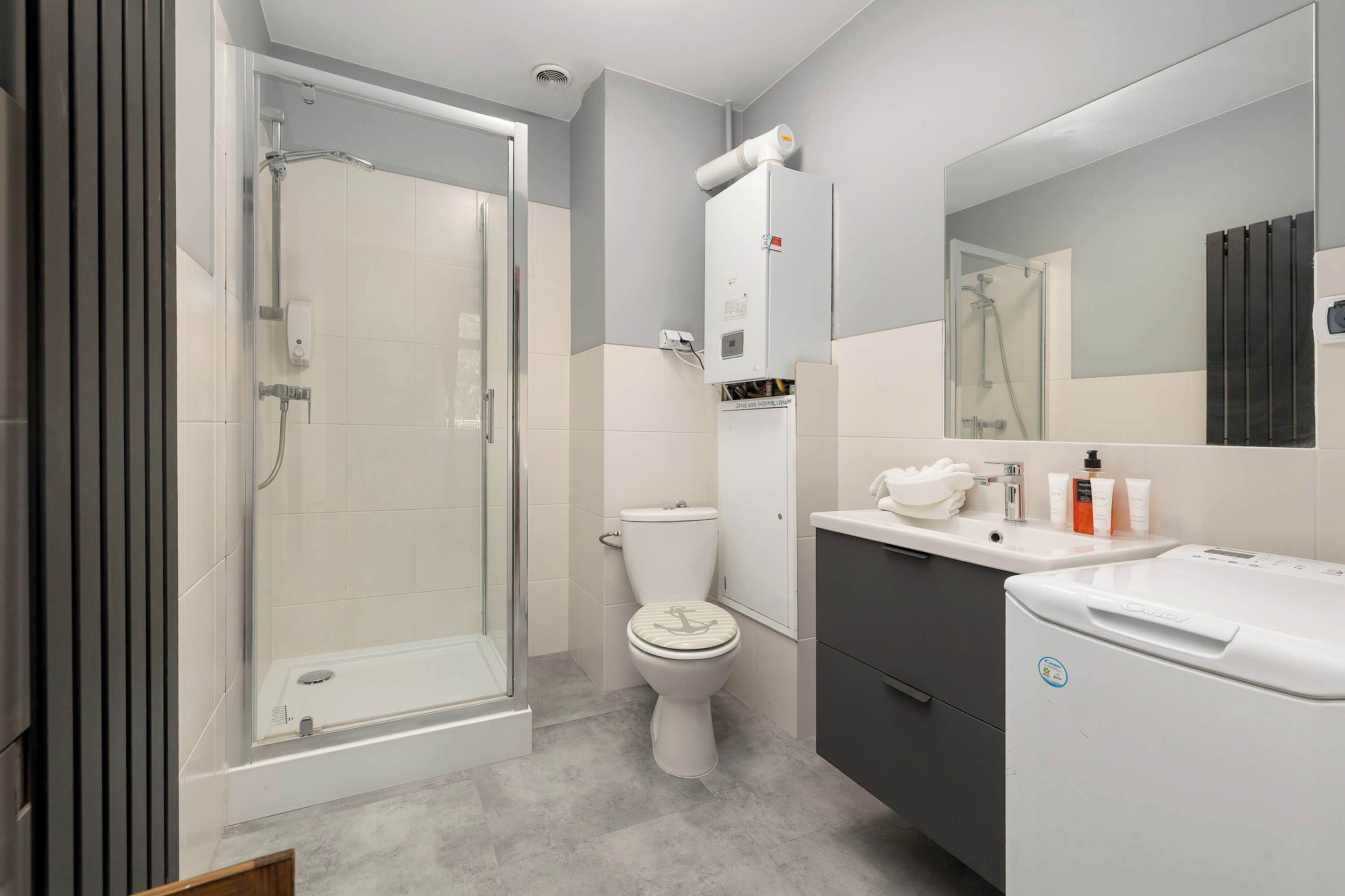 Een moderne badkamer met een glazen douche, toilet en een wastafel met een wasbak en spiegel.