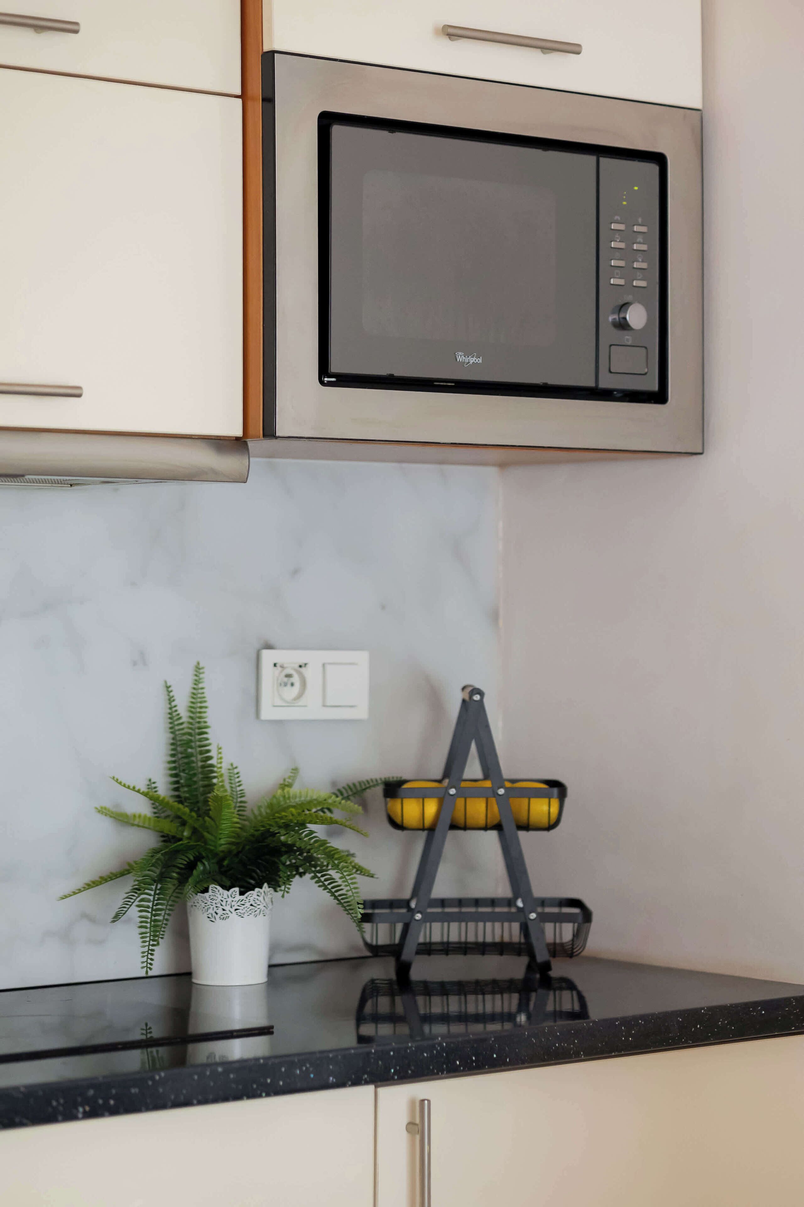 A kitchen with a microwave, a potted plant, and a fruit basket.