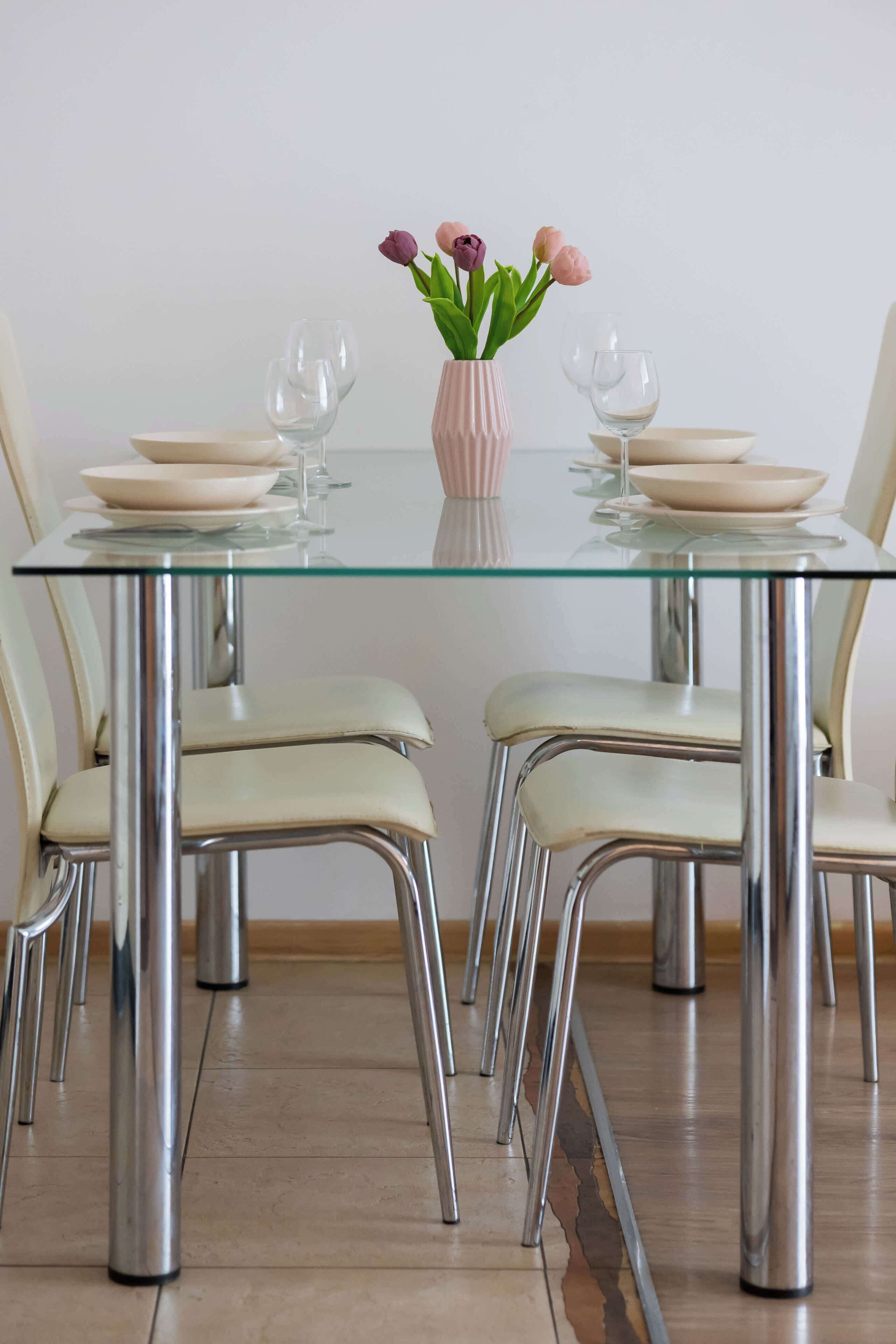 A dining table with four chairs, a vase with flowers, and two wine glasses.
