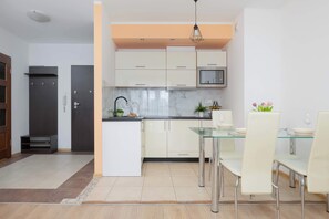 Una cocina compacta con armarios blancos, una mesa de comedor de vidrio y una lámpara colgante moderna.