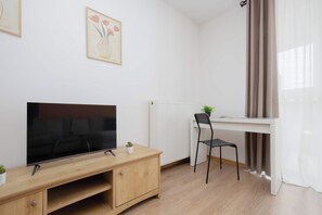 Un salón moderno con un televisor de pantalla plana sobre un mueble de madera, una silla de oficina negra, un radiador y una ventana con cortinas.