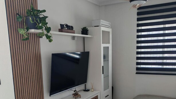 Una sala de estar moderna con un televisor de pantalla plana, un ventilador de techo y una ventana con persianas.