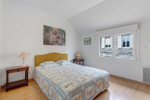 Une chambre à coucher avec un lit, deux tables de chevet, une fenêtre avec des volets et un tableau accroché au mur.