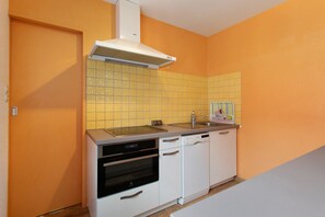 A compact kitchen with a white oven, dishwasher, and a sink with a modern faucet. - "Plouha" Apartment with Balcony and Wi-Fi (Plouha)