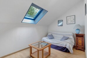 A bedroom with a sloped ceiling, a bed with striped bedding, a small table, a lamp, and framed pictures on the wall. - "Plouha" Apartment with Balcony and Wi-Fi (Plouha)