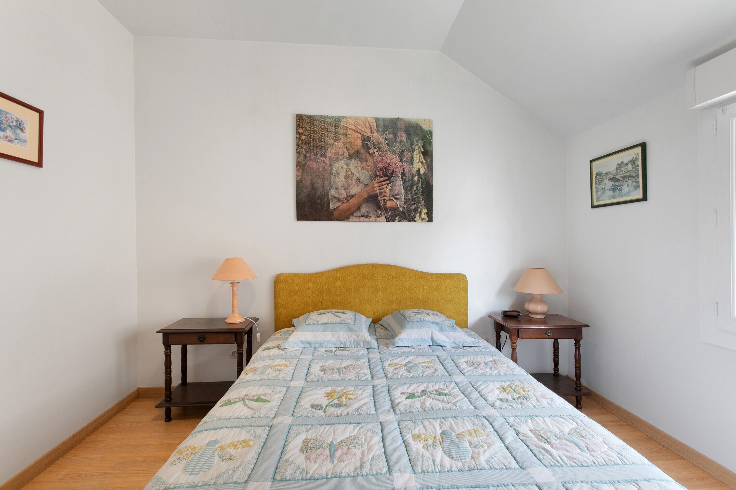 Une chambre à coucher avec un lit, deux tables de chevet, une lampe sur chaque table, un tableau au mur et une fenêtre.