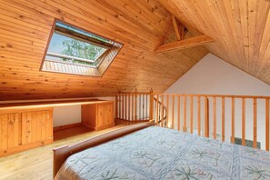 Une chambre avec un plafond en pente, un puits de lumière, un lit, un bureau et un escalier.