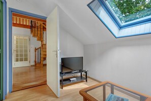 Une pièce avec un escalier en bois, une télévision et une lucarne.