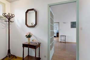 Un couloir avec un porte-manteau, un miroir, une petite table sur laquelle est posé un vase de fleurs et une porte qui donne sur une autre pièce.
