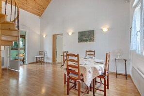 Un coin repas avec une table et des chaises en bois, un tableau au mur et un escalier.