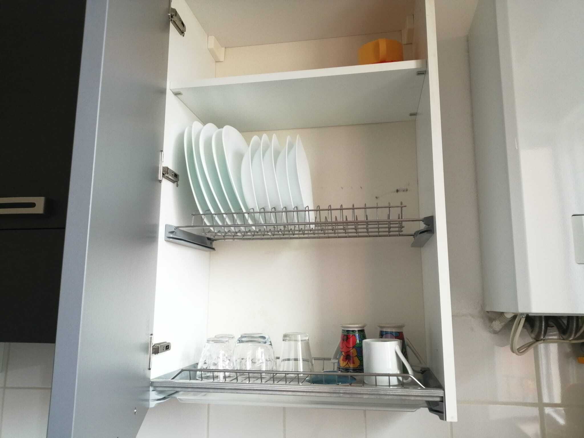 A kitchen with a dish rack, a shelf with glass jars, and a cabinet.