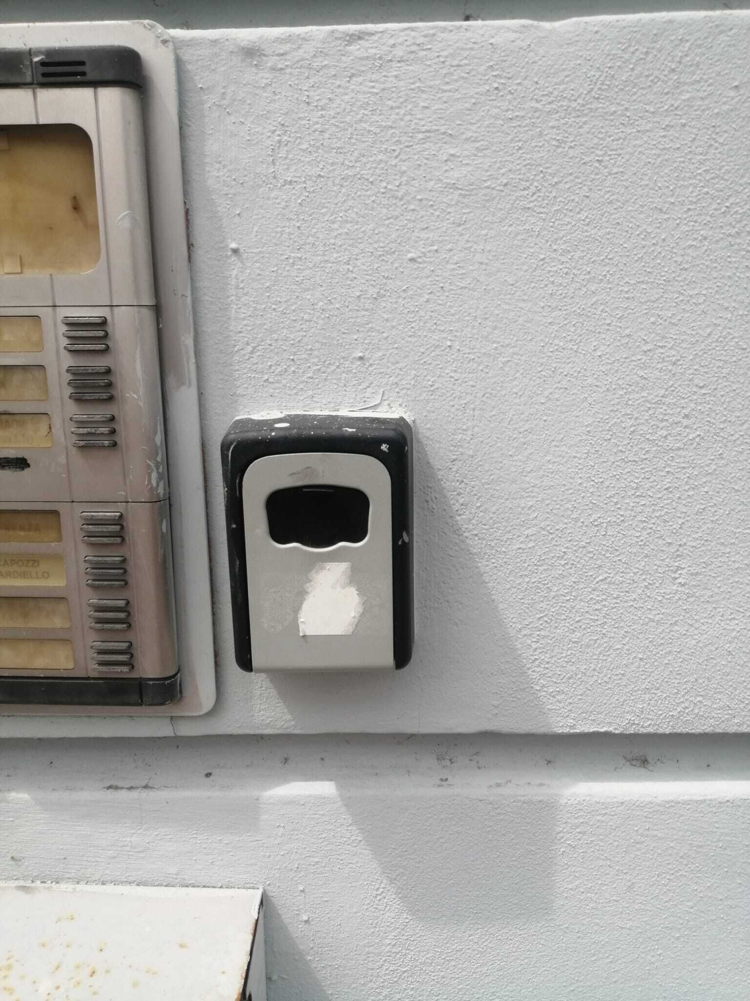 Un mur blanc sur lequel on aperçoit un objet rectangulaire qui ressemble à un interrupteur ou à un panneau de commande.