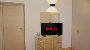 Una stanza con una televisione su un mobiletto in legno, una porta e un punto luce fissato al muro.