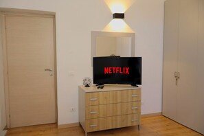 A room with a television on a wooden cabinet, a door, and a wall-mounted light fixture.