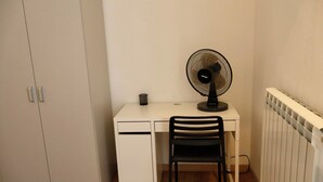 Un'area di lavoro piccola e funzionale, con scrivania, sedia e una ventola da pavimento.