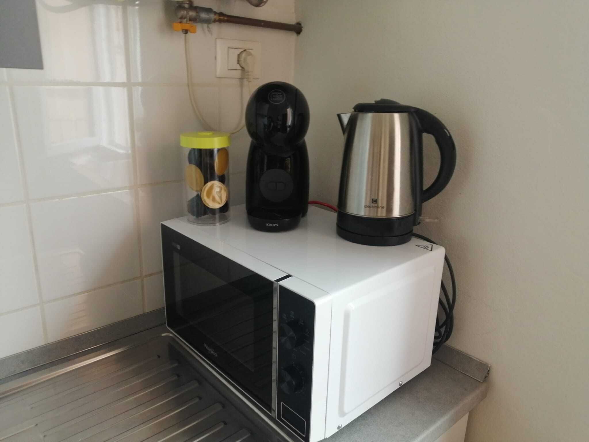 Un four à micro-ondes blanc, avec une cafetière noire et une bouilloire électrique en acier inoxydable posées sur le dessus.