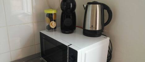 Un four à micro-ondes blanc, avec une cafetière noire et une bouilloire électrique en acier inoxydable posées sur le dessus.