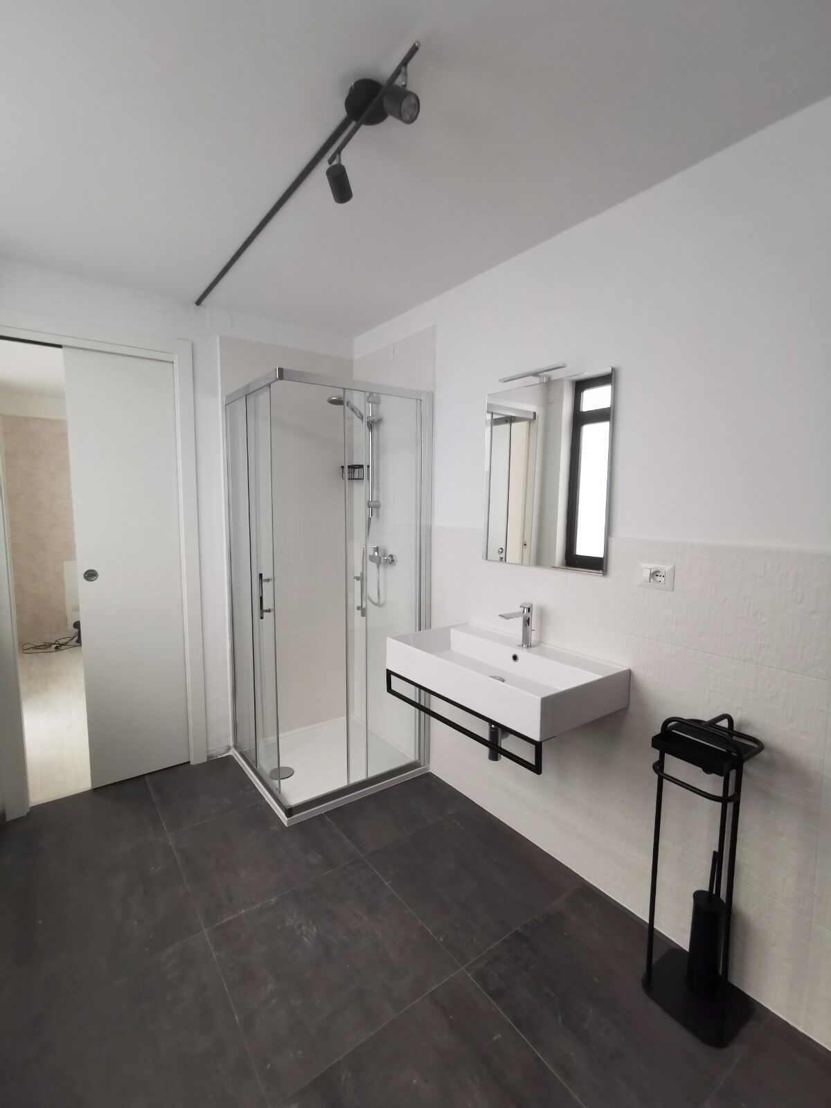 A modern bathroom with a glass-enclosed shower, a white sink with a black frame, and a mirror above it.