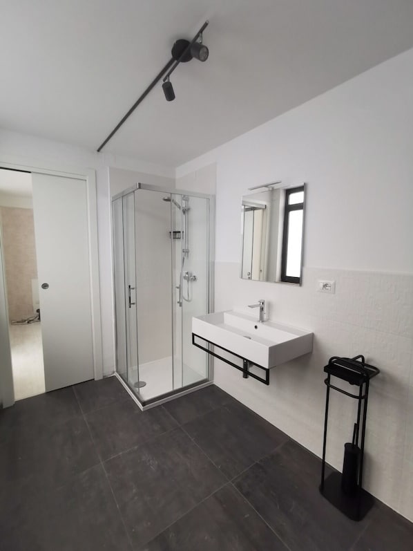 Un baño moderno con cabina de ducha acristalada, un lavabo blanco con marco negro y un espejo encima.