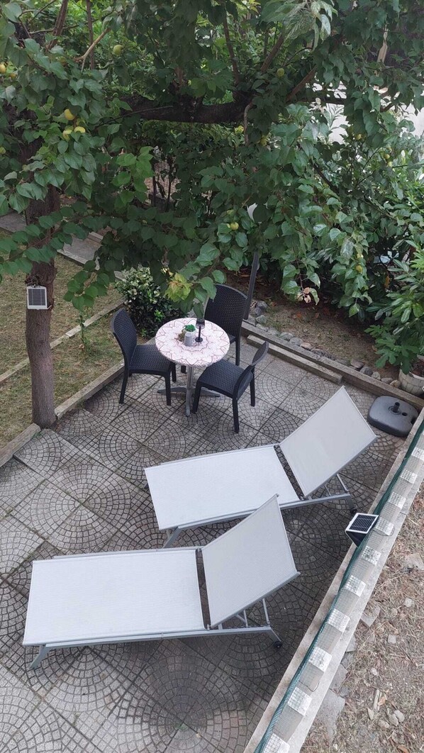 An outdoor seating area with a round table and chairs, surrounded by a garden with trees and a paved floor. - Giulianova Suite, 600 meters from the beach, with convenient parking (Giulianova)