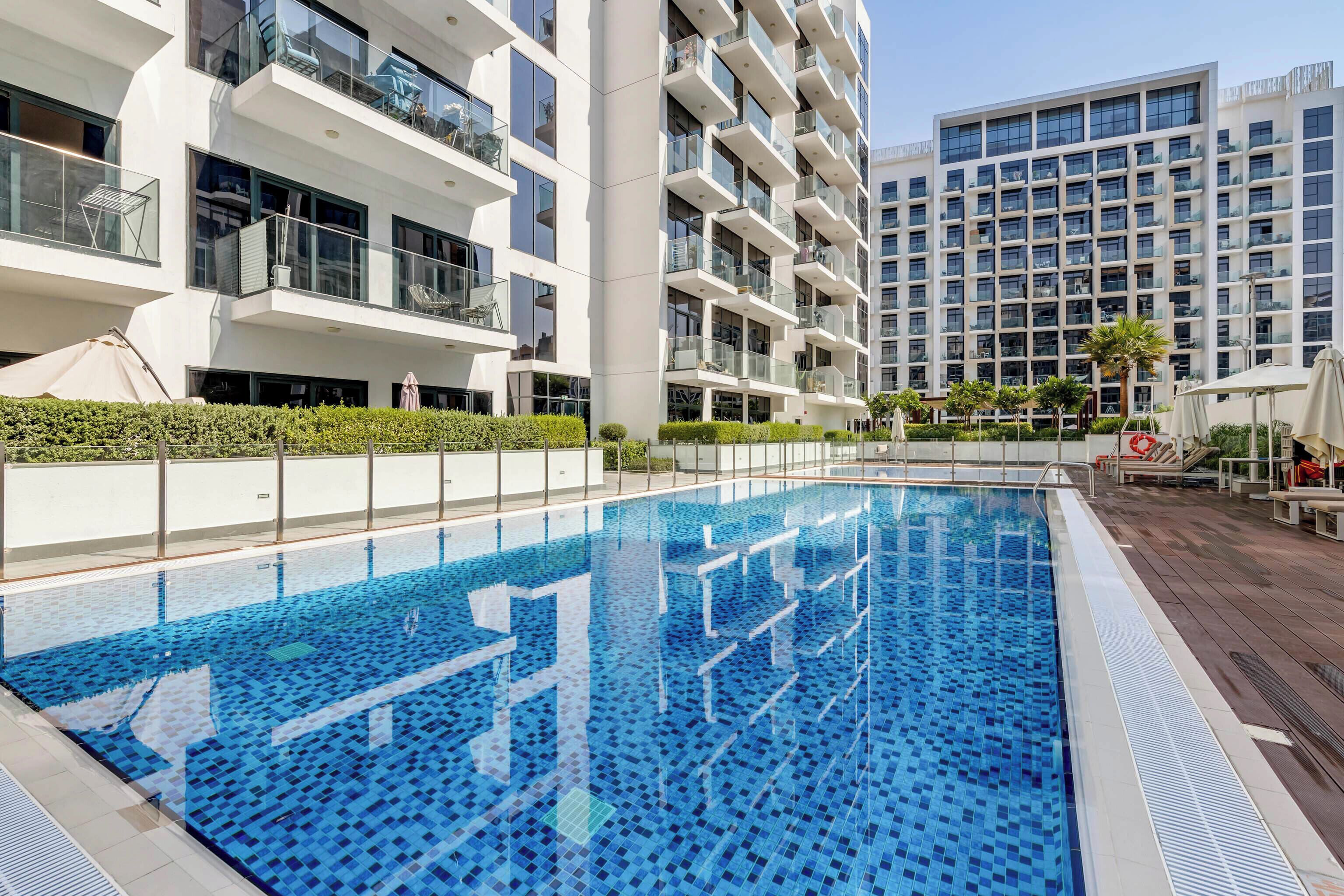 A modern residential building with a swimming pool, balconies, and a clear sky.